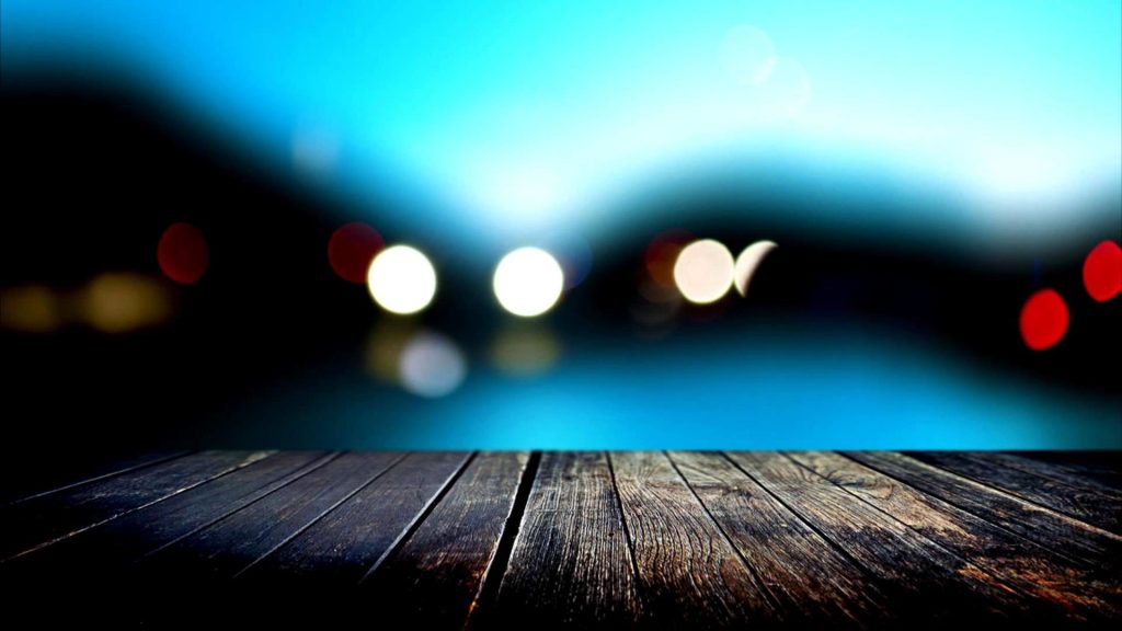 A blurry view of a lake and lights in the background with a close up view of a wooden deck in the foreground